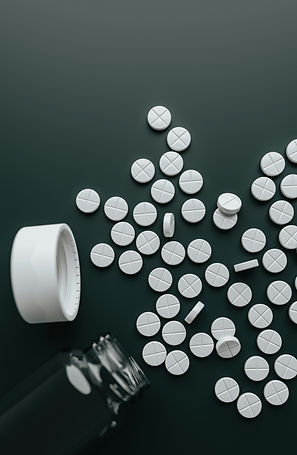 White tablets spilled from an open pill bottle onto a dark surface, creating a stark, high-contrast scene.