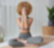 A young woman in her 20s, sits on a yoga mat, wearing yoga wear, sits in the childs pose with her hands folded in front of her face.