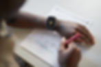 An image of a young man, sitting at a desk, about to work on a test. His smart watch shows the THRIVE app, which he has marked his notification to go to the test as complete.