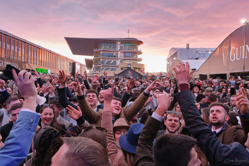 a view over the crowds in the Guinness village at cheltenham racecourse with a red sunset