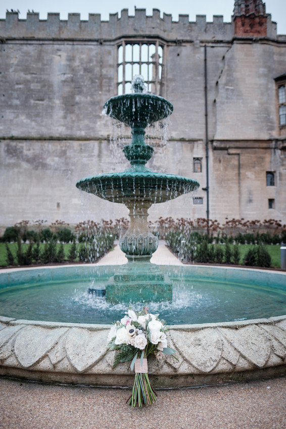 a brides bouquet stood next to a fountain in Thornbury castle courtyard