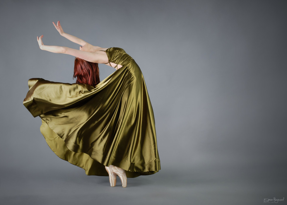 girl wearing green flowing dress arching her back while en poite in ballet shoes