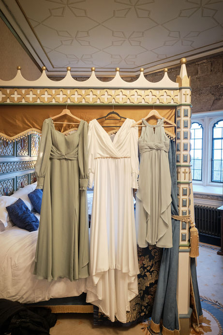 a bride and bridesmaids dresses hung on a four poster bed