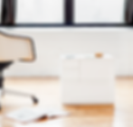 White chair and drawers in a bright room with wooden floor. An open magazine lies on the floor, glasses and phone on the drawers.