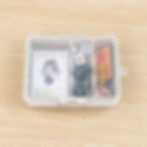 Box with a trading card featuring an anime character, dice, tokens, and cards on a light wood table. Contains stars and number icons.