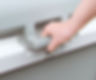Hand gripping a grey plastic handle on a container, with a simple background. Neutral mood, no text or patterns visible.