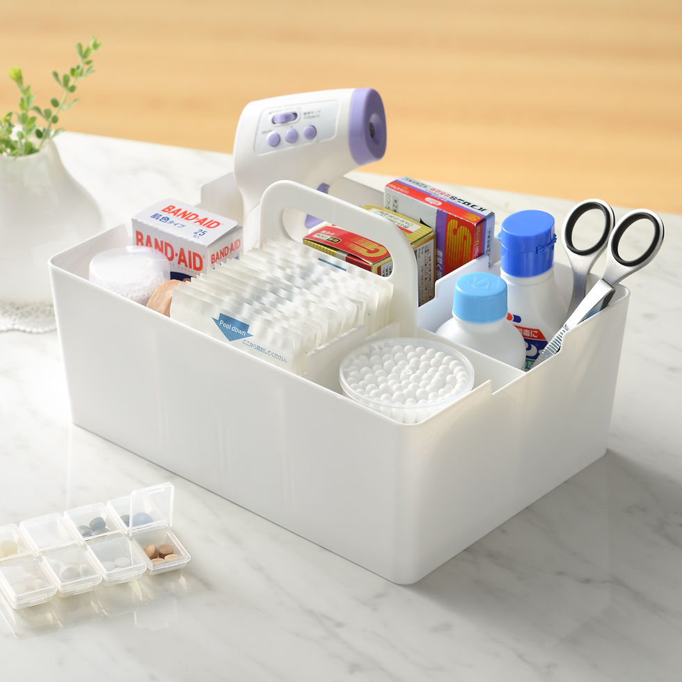 White organizer with first-aid items: bandages, thermometer, wipes, medicine, scissors. Set on a marble table with a plant nearby.