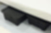 Black storage bins under a bed on a light carpet, against a white background. No visible text; a tidy and organized setting.