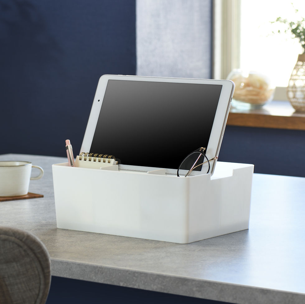 Tablet in white organizer with glasses, notebook, and pencil on a light grey table. Background is navy and white, with window light.
