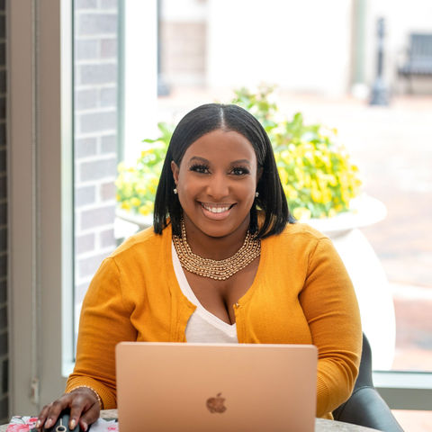 Lady in yellow on computer smiling at camera