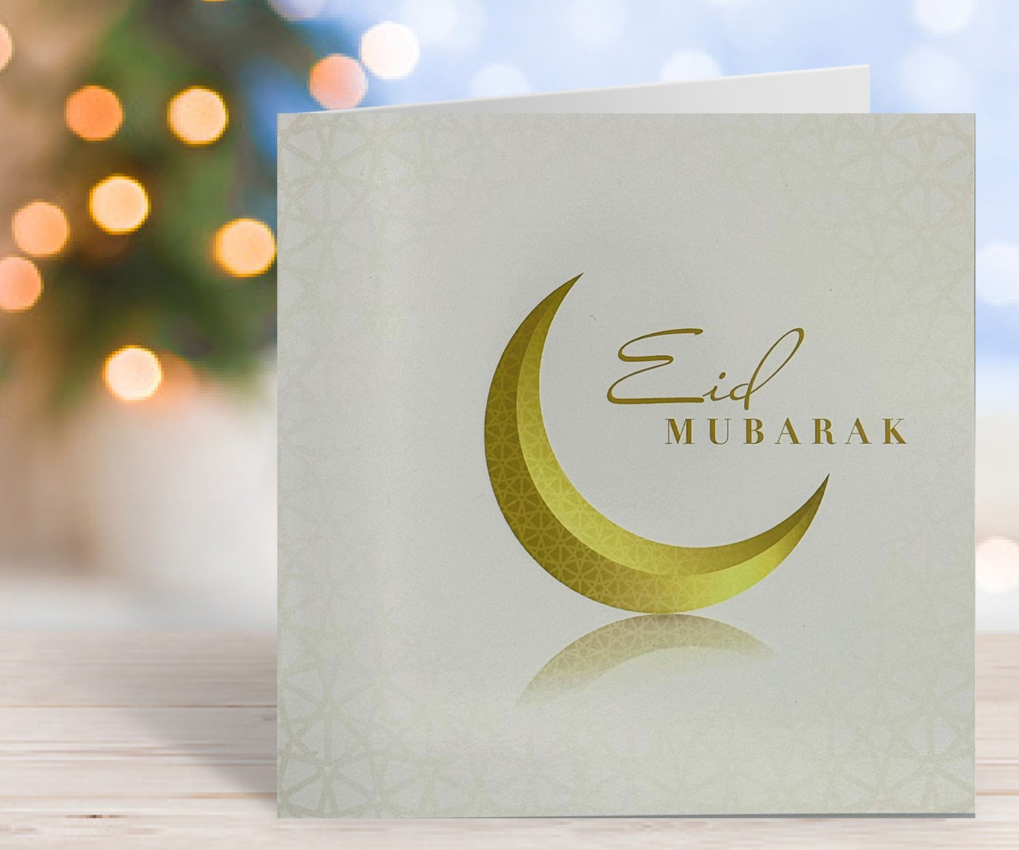 White Eid Mubarak card light gold crescent moon with fairy lights in the background