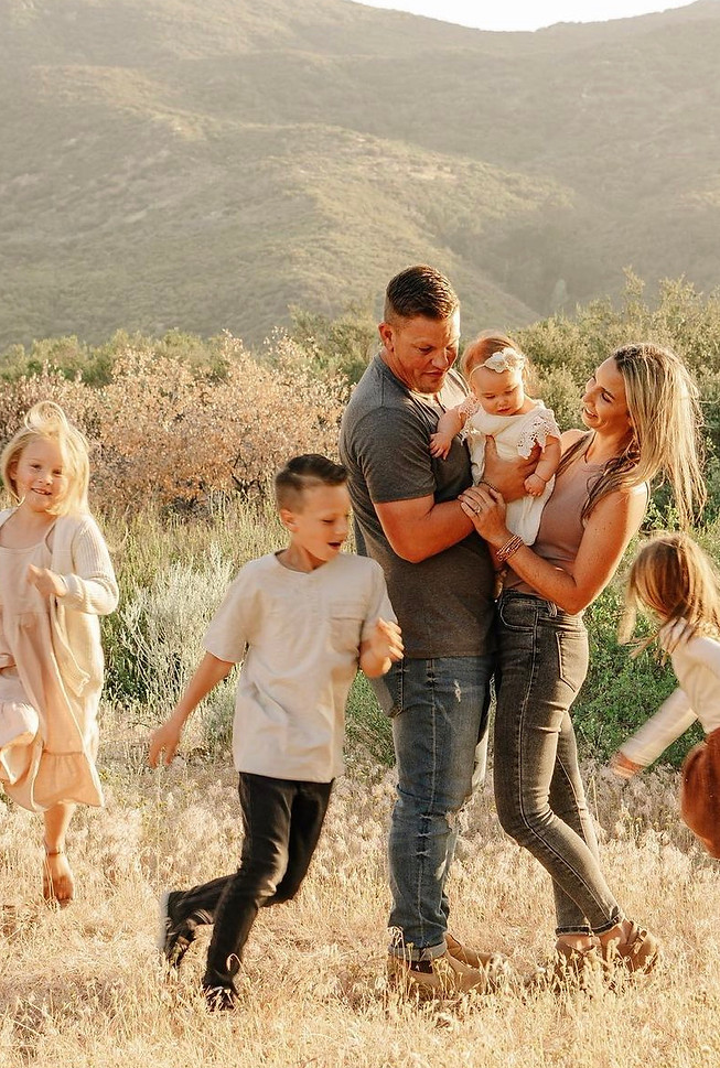 Family photo with a husband and wife holding a baby, while their other children run around them playfully.
