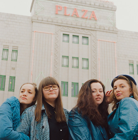 A photo of The Deep Blue dressed in blue shades in front of a tall building white building.