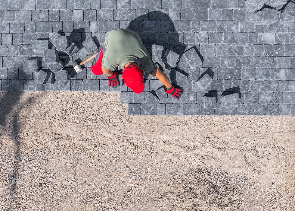 A laborer carefully positions paver stones to create a sturdy driveway in a residential se