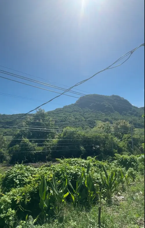 Wide roadside view of green land between El Tunco and Tamanique in El Salvador, showing open area and nearby jungle hills.
