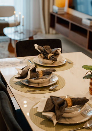 Dining table place setting — woven placemats, brown linen napkins, brass napkin rings, on marble-look table