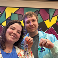 Smiling couple holding colorful custom keychains against a vibrant abstract wall.