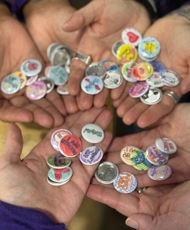 Several hands holding many small colorful buttons, one clearly says Pandora.