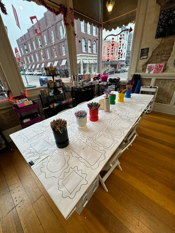 Long table with coloring pages and art supplies in a studio.
