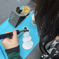 Child soldering a snowman circuit board on a blue mat.