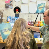 Woman painting at easel as man assists in art studio class.