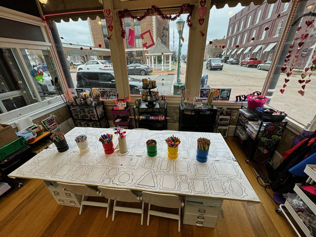 Long coloring table with art supplies in bright studio overlooking street.