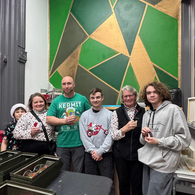 Group of five smiling people, "KEEPIN' IT JOLLY" shirt, green geometric mural.