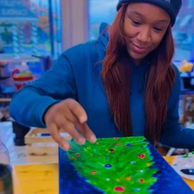 Young woman in "ART + DESIGN" hat focused on painting vibrant canvas.
