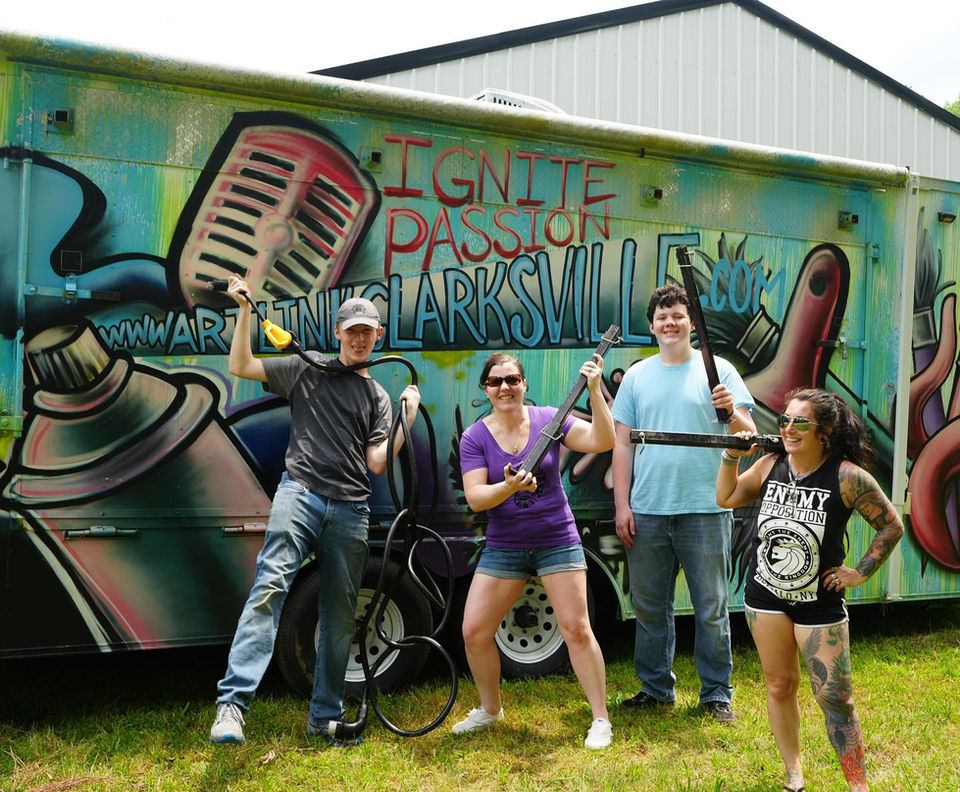 Four people hold metal art before IGNITE PASSION IN CLARKSVILLE painted trailer.