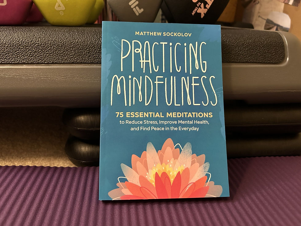 A copy of 'Practicing Mindfulness' by Mathew Sockolov resting on a purple yoga map with a step up and multicolored hand weights in the background
