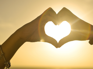 mãos unidas em formato de coração com o sol ao fundo