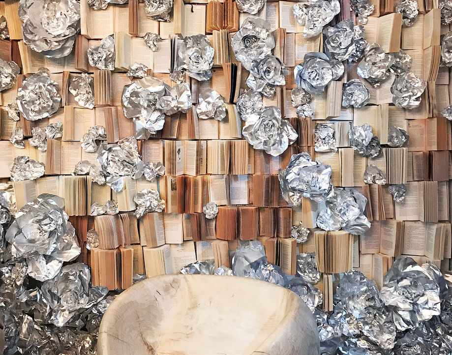XL art installation by multimedia artist Katja Müller AJTAK with books and aluminum foil flowers mounted on wall.