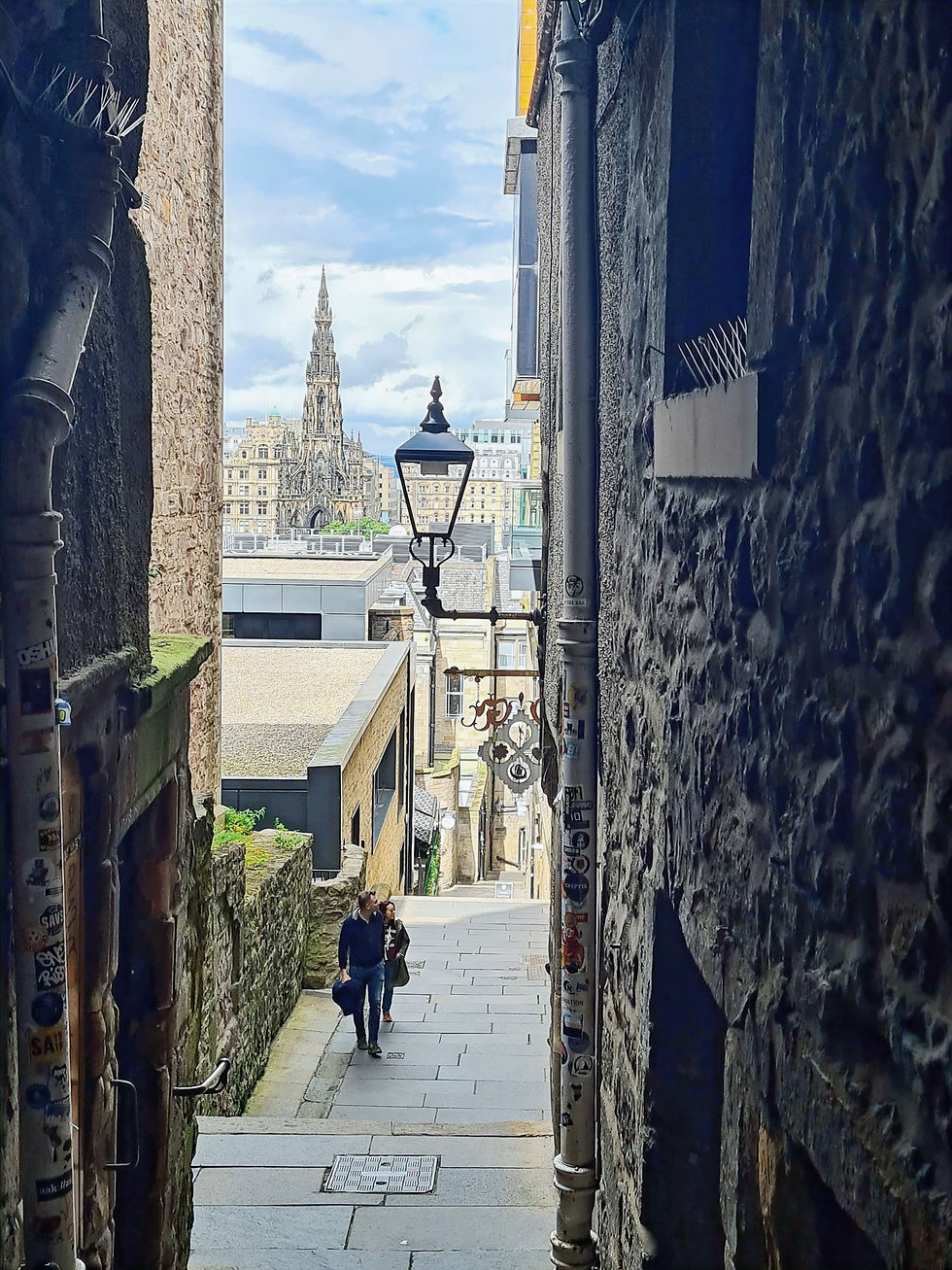 Narrow close in Edinburgh old town with stone walls, gas lamp, and Scott Monument visible in the distance, Scotland