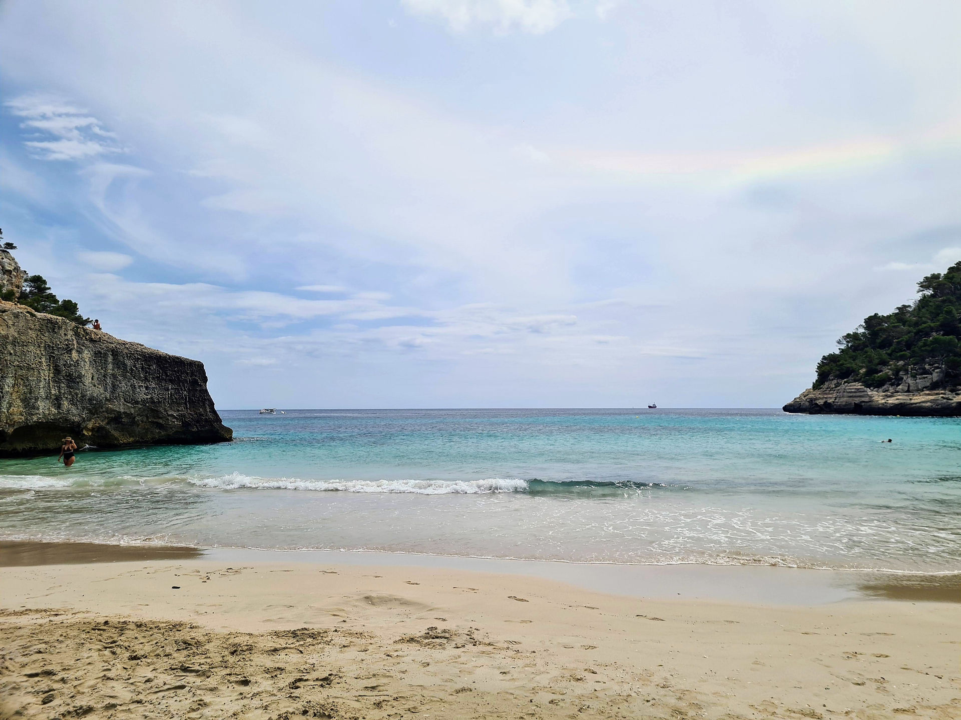 View of Platja Mitjana, a secluded cove with turquoise water, white sand, and pine trees