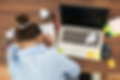 A person slumps forward over a desk, their head on their arm, which rests on a spiral notebook. Around them are many pieces of crumpled up paper. Sticky notes are scattered everywhere across the desk and the nearby laptop. The impression is that the writer is frustrated.