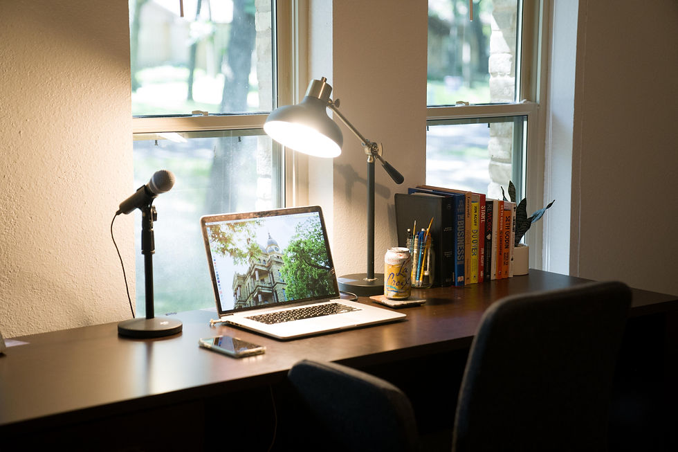 A desk in a room with a laptop, books, lamp, and a microphone on the desk