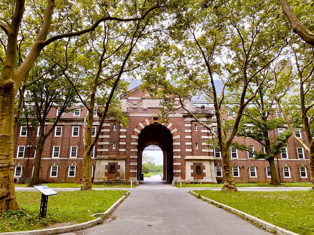 Exterior view of Liggett Hall, a massive bracket-shaped building with a tall archway toward the center, located in Governors Island, New York.