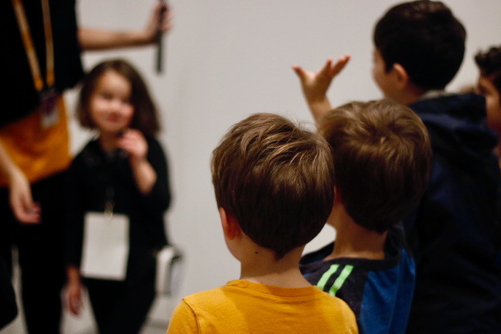 A young boy raises his hand to offer his comments, actively participating in a kid-led public tour.