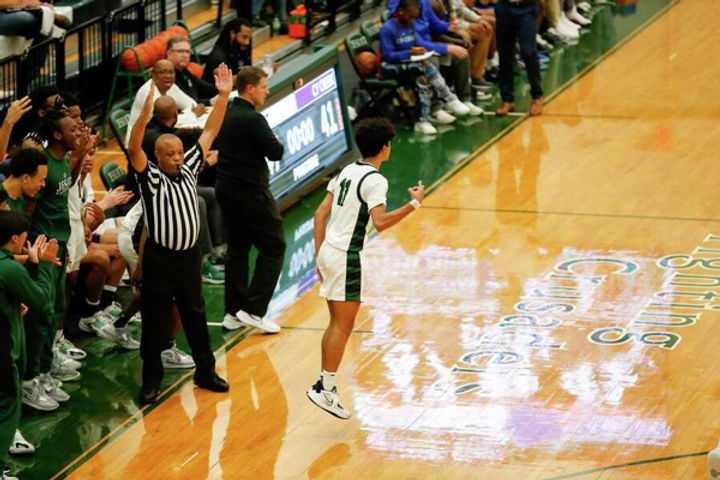 A victorious basketball player celebrating on the court, with teammates and coaches in the background reacting with excitement during a game.