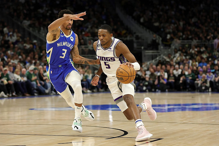 A Sacramento Kings player dribbles the basketball while being closely defended by a Milwaukee Bucks player during a game.