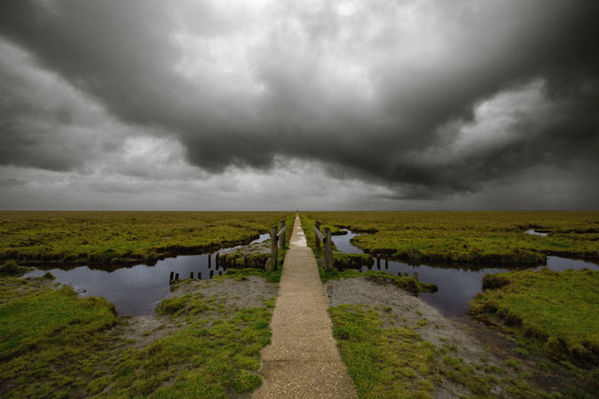 Steg durch Marschland unter Gewitterwolken