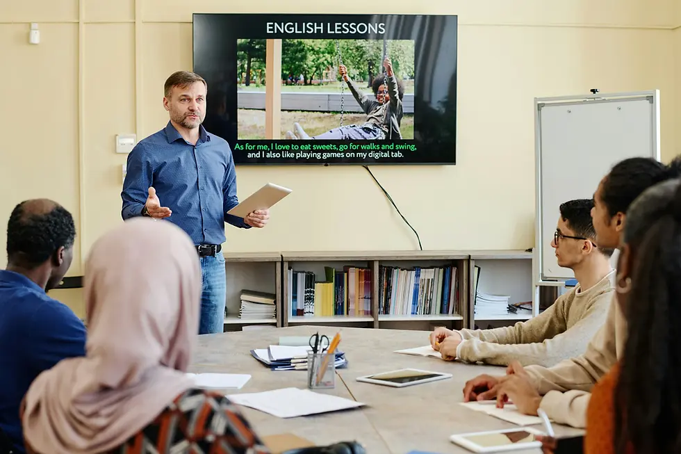 What is the easiest language to learn? - Man standing in front of class next to TV with English lessons slideshow
