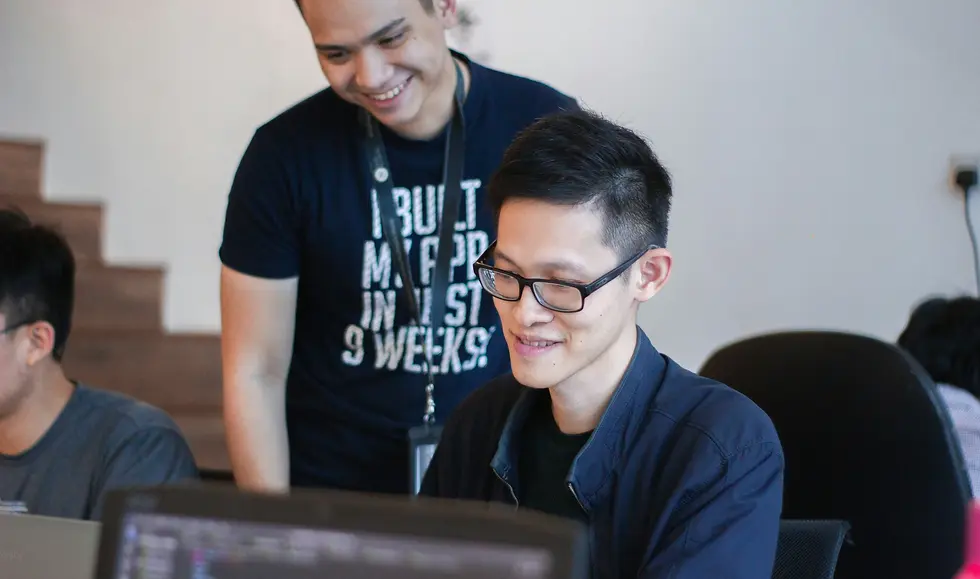 Tutor helping male student on laptop in class