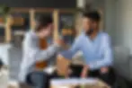 Down syndrome male student holding a book open and shaking hands with a male tutor who is smiling at him
