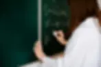 Teacher writing math equation on green chalk board
