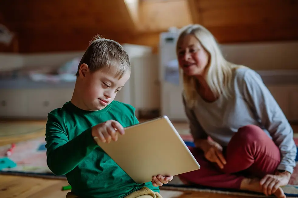 Photo of a young down syndrome boy using a tablet while his mom watches