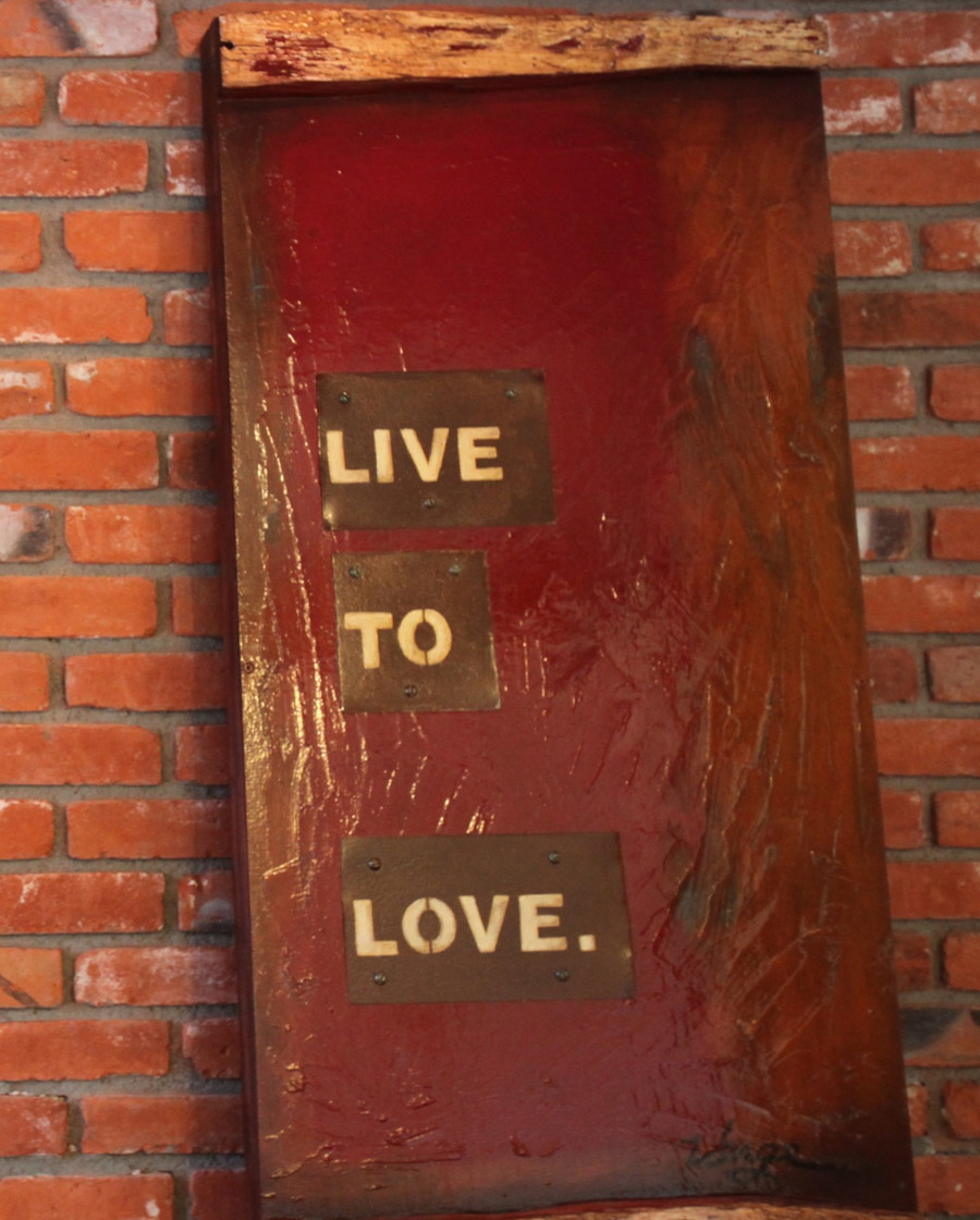 A weathered red door in the brick wall with brass plaques reading LIVE TO LOVE