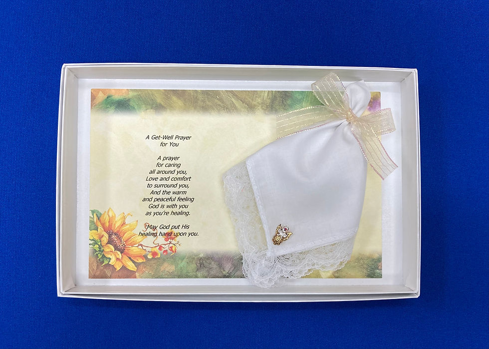 A white box with a card with a sunflower border and a printed poem, alongside a white hankie adorned with an angel pin.