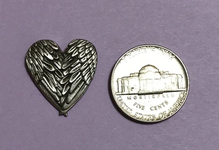 Thumbnail: A delicate heart pin adorned with angel wings, symbolizing love and protection along side a nickel.