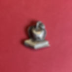 An antique silver apple on a book pin on a red background.